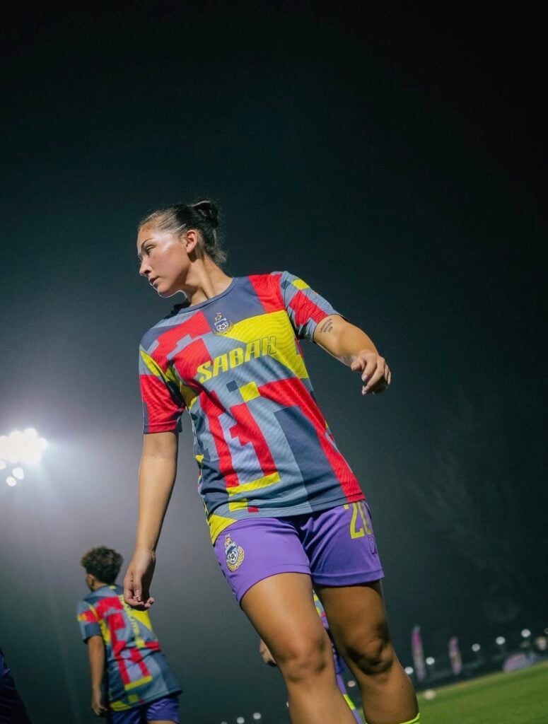 Professional women’s soccer player in a Sabah FC kit walking on the pitch under stadium lights